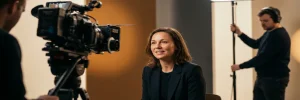 Zelfverzekerde professional voor een cinema camera op moderne filmset, verlicht door warm sleutellicht, bemanningslid zichtbaar op de achtergrond.
