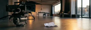 Professionele videocamera op statief in Amsterdamse studio met verfrommeld document op betonvloer, cinematografische belichting.