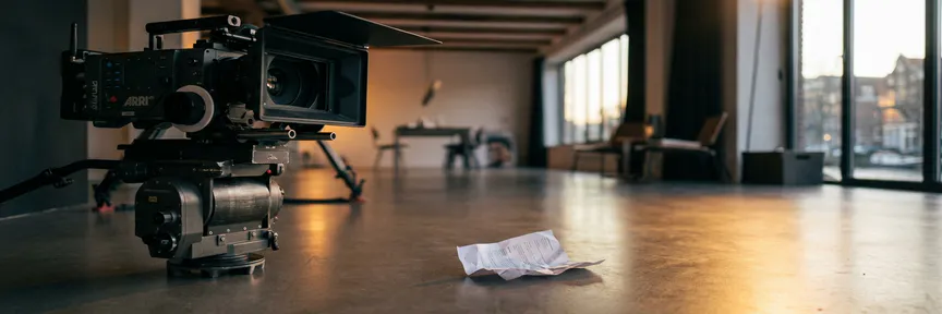 Professionele videocamera op statief in Amsterdamse studio met verfrommeld document op betonvloer, cinematografische belichting.
