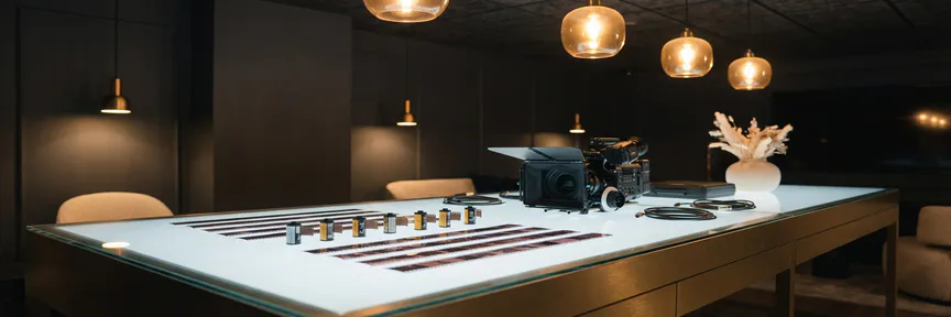 Gerangschikte branded videoreels op een verlichte lightbox tafel naast een cinema-camera, in een professionele B2B-videostudio met warm amber licht.