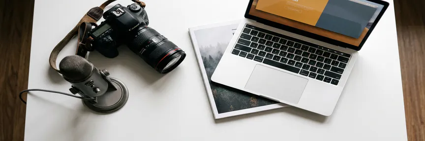 Professionele camera, microfoon, tijdschrift en laptop op wit bureau als flat lay met warme en koele tinten.