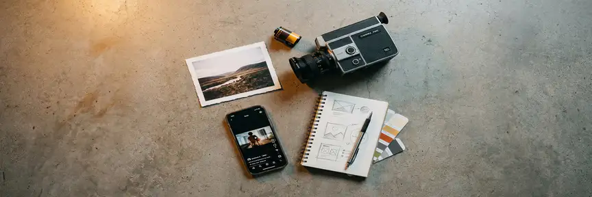 Flatlay van diverse contentformaten: filmcamera, foto, smartphone met videoframe en schetsboek op betonnen ondergrond.