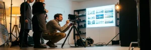 Fotograaf stelt camera op statief in Amsterdamse studio, met gloeiende lightbox op achtergrond en warme amberkleurige studioverlichting.