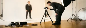 Fotograaf stelt spiegelloze camera op statief in Amsterdams studio in, met wit achterdoek, verlichtingsset en lenscases op betonnen vloer.