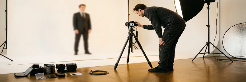 Fotograaf stelt spiegelloze camera op statief in Amsterdams studio in, met wit achterdoek, verlichtingsset en lenscases op betonnen vloer.