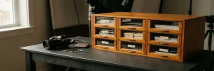 Houten lightbox-ladekast met gelabelde fotoafdrukken en contactvellen naast een spiegelloze camera, geheugenkaarten en harde schijf op studioburo.