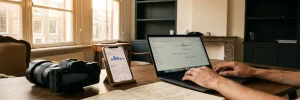 Socialmediamanager werkt aan bureau met camera, smartphone met analysegrafieken en contentplanning in warm Amsterdams studiolicht.
