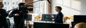Videoproductieteam filmt een softwareontwikkelaar in een modern Amsterdams kantoor met monitors en technische apparatuur op de achtergrond.