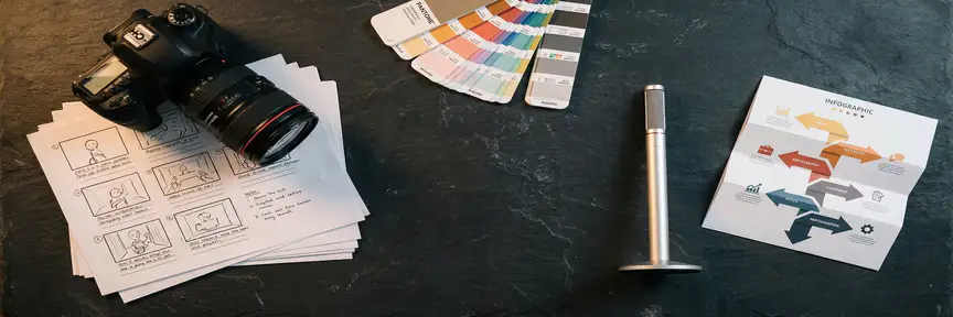 Professionele camera, storyboard-vellen, kleurenwaaier en microfoon als flat lay op donker leisteen bureau met warme studiobelichting.