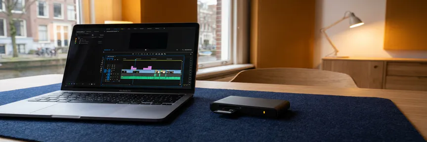 Laptop met videotijdlijn naast geheugenkaartlezer op een opgeruimd bureau in een Amsterdams videobewerkingsstudio.