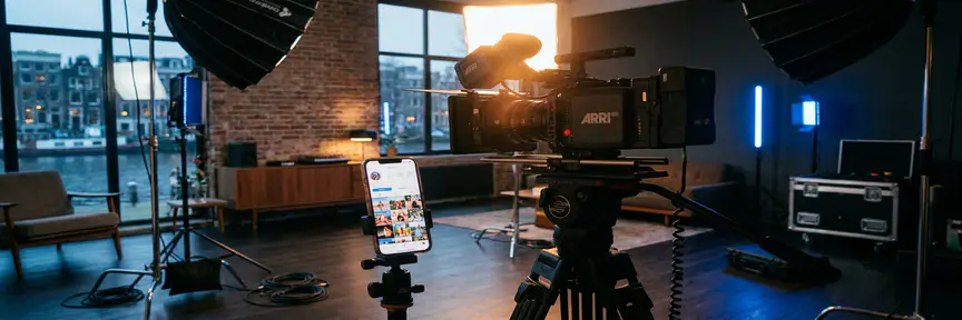 Professionele videocamera op statief gericht op smartphone met social media feed in Amsterdams studio met softboxen en cinematische belichting.