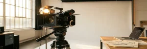 Professionele videocamera op statief in verlicht Amsterdam-studio met wit achtergrond, storyboard-schetsen en laptop op bureau.