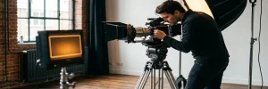 Videograaf stelt cinema camera op statief in in Amsterdams studio met warm amberkleurig licht en regisseurmonitor op de achtergrond.
