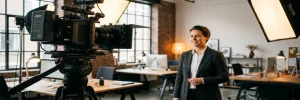Professionele videocamera op statief gericht op een zelfverzekerde zakenman in een modern Amsterdams studio met warme sfeerverlichting.
