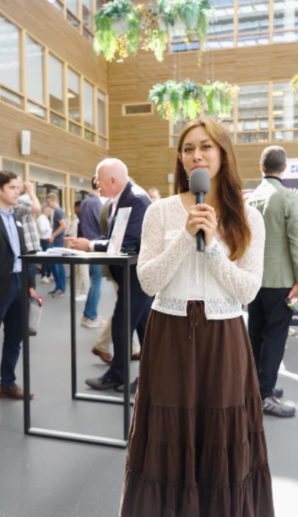 Vrouw met microfoon neemt interview op in zaal en kijkt camera in