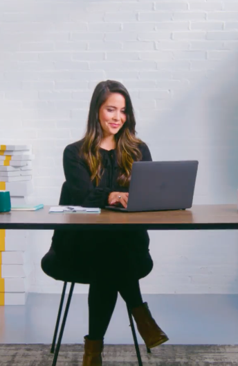 Mevrouw zit aan tafel te werken achter haar laptop